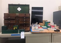 Overall view of wooden chest on cabinet with green plastic bit cases and assorted hardware laid out