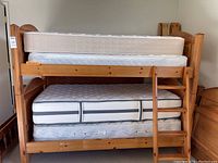 Front view of the assembled wooden twin bunk bed with two mattresses stacked on each bed level, showing the ladder on the right side