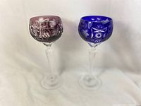 Pair of Nachtmann Traube Ajka crystal Marsala wine glasses side by side, one cobalt blue and one amethyst, showing their height and cut crystal etched design.