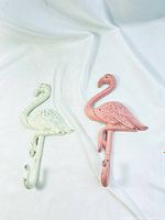 Pair of metal flamingo hooks, one pink and one white, laid on a white cloth background.