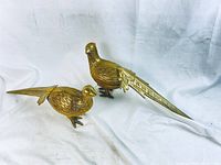 Two large brass pheasant figurines, one male and one female, side by side on white background.