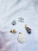 Five assorted pendants and charms laid out on a white cloth, showing variety of materials and styles.
