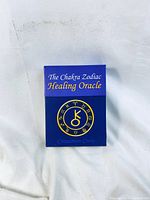 Front of original box for The Chakra Zodiac Healing Oracle by Cinnamon Crow, blue with gold and white text and a circular zodiac emblem.