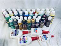 Multiple bottles of craft paint in assorted colors with four bottles of white glue in front
