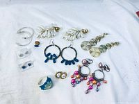 Top view showing ten pairs of earrings in various designs and colors alongside a blue jewelry ring with flower detail.