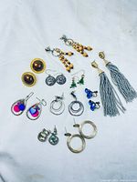 Overview of all earrings laid flat on white fabric showing all pairs and their styles and colors.