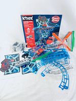 Box and all K'NEX pieces laid out including blue track pieces, orange connectors, green rods, black structural parts, and packaging showing K'NEX Thrill Rides graphics.