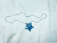 Full view of the sterling silver chain necklace with blue glass starfish pendant laid out flat on white fabric.