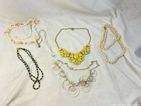 Lot of seven necklaces on white background, including beaded, metal, and faux pearl designs.
