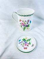White ceramic mug and matching trivet/lid with colorful sweet peas and butterfly design, showing full set.