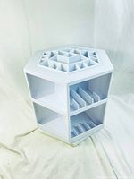Front view of white hexagon rotating makeup/craft caddy with multiple compartments including triangular dividers on top and vertical slots below.