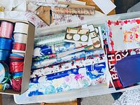 Top view of open bin showing rolls of wrapping paper, ribbons in spools, gift bags, and stickers inside