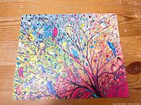 Completed laser cut wooden puzzle showing numerous colorful birds on tree branches. The image is artistic with vibrant pastel colors and intricate patterns.