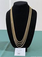 Full view of the four connected gold-tone flat chains displayed on black bust stand