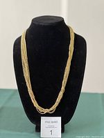 Full view of 8 strand gold-tone seed bead necklace displayed on black bust stand.