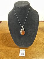 Front view of the Baltic amber pendant on a black mock neck display stand, showing the amber stone and silver-tone grape and leaf design.