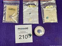 Lot arranged on purple fabric showing three small opal slices in plastic bags, one larger opal in round case, and a small opal pin with silver-tone setting.