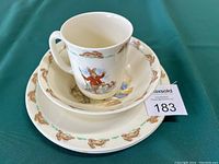 Stack of Bunnykins cup, cereal bowl, and small plate showing illustrated rabbits and border design of running bunnies.