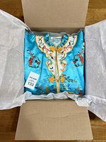 Turquoise embroidered Chinese robe jacket folded in box with white tissue paper