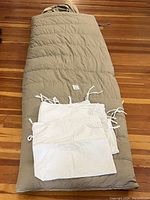 Image of beige side of sleeping bag laid flat with two white cloth liners on top.