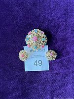Full set of gold-tone filigree brooch and matching clip-on earrings on purple background with lot number tag.