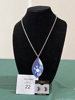 Blue enamel pendant necklace and Alaskan Black Diamond earrings displayed on black jewelry bust with lot number card.