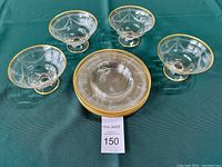 Top view of four dessert bowls arranged around five stacked plates, all with gold rims and etched patterns