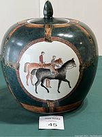Front view of dark green porcelain ginger jar showcasing two equestrians on horses inside a circular frame with bridle decorations around.