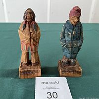 View of two painted wooden Huron Indian carvings, showing detailed facial features, clothing, and bases labeled Malbaie.