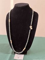 Front view of necklace, dark grey pearls with cream pearl and rhinestone accents displayed on black bust form.