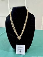 Full view of Kramer necklace displayed on black bust with four gold-tone chain strands and attached round pendant
