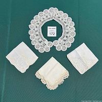 Top view of lace collar centered above three lace-trimmed handkerchiefs arranged in a fan shape on a green fabric background.