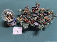 Photo showing both items in the lot: the Nativity musical snow globe and the artificial evergreen votive centerpiece.