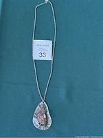 Full view of the pendant necklace lying flat on a teal fabric background with auction lot label.