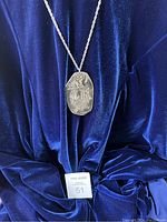 Front view of the pewter pendant necklace against blue velvet background, showing detailed artistic embossed design.