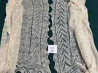 Two cream colored square wool wraps with lace knit patterns, one folded showing soft texture and edges
