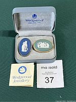 Two Wedgwood cameo brooches in original Wedgwood-branded case with soft grey lining, also showing Wedgwood Jewellery tag and MaxSold lot number 37.