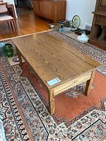 Wooden rectangular coffee table with a natural brown wood grain finish, placed on a patterned rug with water marks and stains visible on the tabletop.