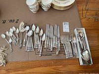 Layout of the full silverware set including knives, forks, tablespoons, teaspoons, a pie server and serving spoons all with floral detail on handles.