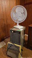 Holmes white oscillating fan on top of General Electric dehumidifier, brown wood panel walls background