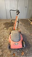 Front-facing photo of the lawnmower showing the Black & Decker label on the plastic deck and the orange extension cord wrapped around the handle.