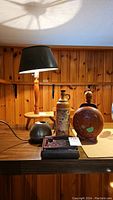 Four vintage items on wood shelf including crock jug, wood carved jug, copper pot, and ashtray under a small lamp