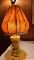 Full view of marble base lamp with orange vintage fabric shade lit from within, showing the general shape and color of the lampshade and base.