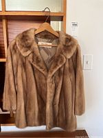 Front view of light brown mink fur coat hanging on wooden hanger, showing collar and fur texture.