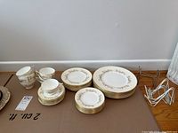 Photo showing arranged plates, saucers, and teacups with a metal plate rack and a white plastic rack on a cardboard surface against a wall.