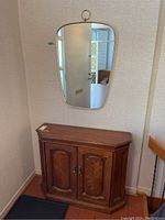 Full view of wood hall table with double doors below and mid-century modern framed mirror with brass ring hanger above, mounted on wall.