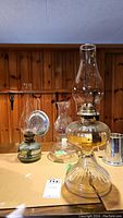 View of three oil lamps and a hurricane candleholder on a table against a wood-paneled wall