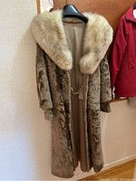 Full view of long Persian lamb fur jacket with large fox fur collar on black hanger against wall and door background