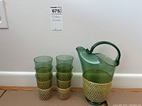 Full view of green glass pitcher with matching green glasses, all featuring rattan netting around the base.