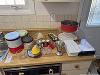 Full view of kitchen items including tins, measuring cup, baking mold, ice cube tray, and various small glass and metal kitchen utensils placed on kitchen counter.